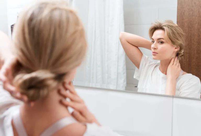 Middle-aged woman looking at signs of aging in a mirror, contemplating anti-aging options.